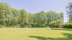 Un espacio al aire libre con césped, un arco de fútbol, árboles y un parque infantil.