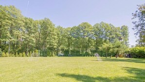 Een gazon met een voetbaldoel, bomen en een speeltoestel.