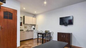 Een kleine keuken met een eethoek, een aan de muur bevestigde televisie en een houten deur.