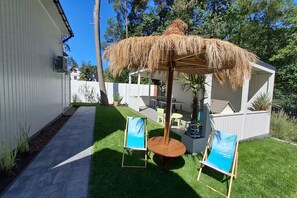 Ein Garten mit einem strohgedeckten Sonnenschirm, einem kleinen Tisch, zwei Stühlen und einem Blumentopf.
