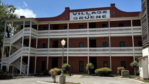 Un edificio a due piani con un cartello che riporta 'Village at Grune'. Presenta una facciata in mattoni, ringhiere bianche e un parcheggio di fronte.