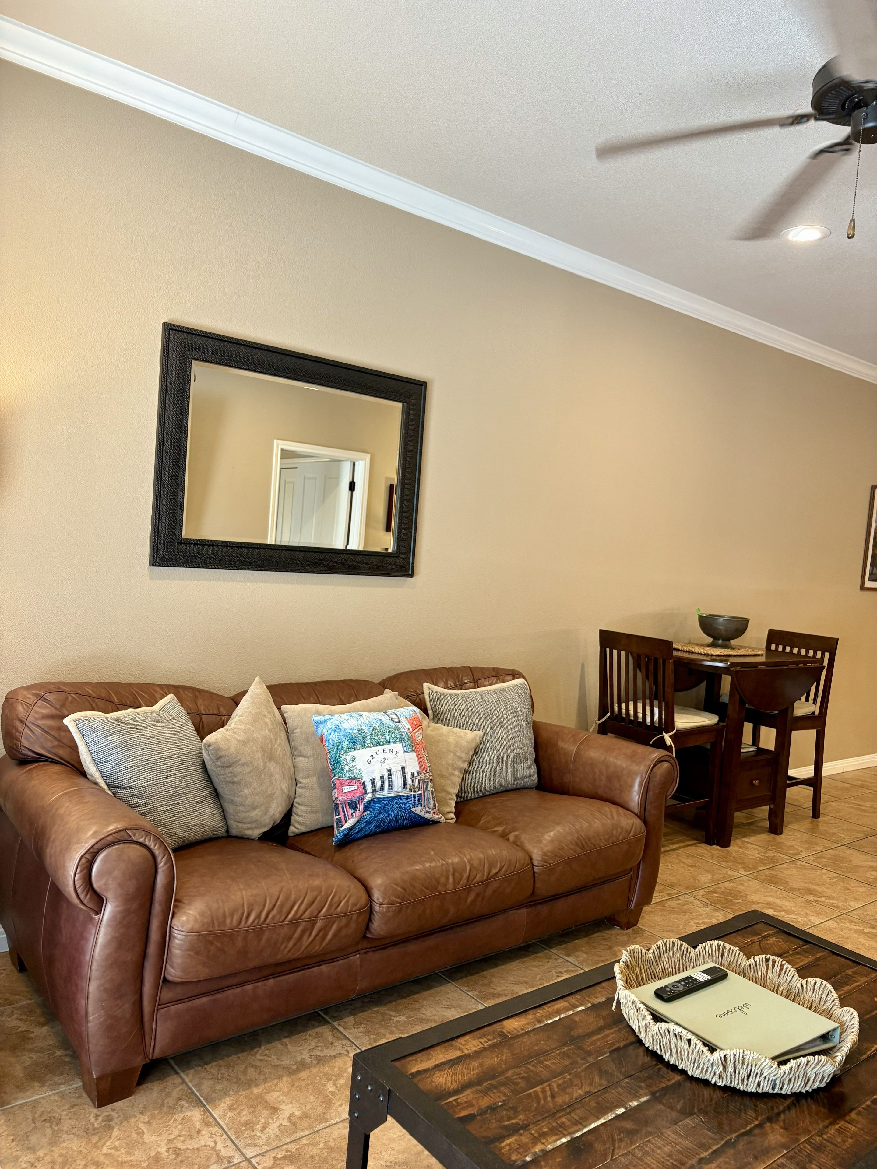 A living room with a brown leather sofa, a coffee table, a dining table with chairs, and a ceiling fan.