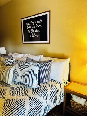 A bedroom with a bed featuring striped bedding, a framed inspirational quote on the wall, and a bedside table with a lamp.