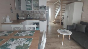 Ett kompakt bostadsutrymme med ett litet kök, en matplats med bord och stolar, en liten soffa och en trappa som leder till ett annat plan.
