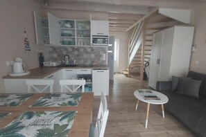 A compact living space with a kitchenette, a dining area with a table and chairs, a small sofa, and a staircase leading to another level. - Comfortable houses with terraces (Pobierowo)