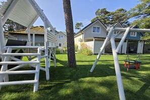 A playground with white play structures, a tree, and houses in the background. - Comfortable houses with terraces (Pobierowo)