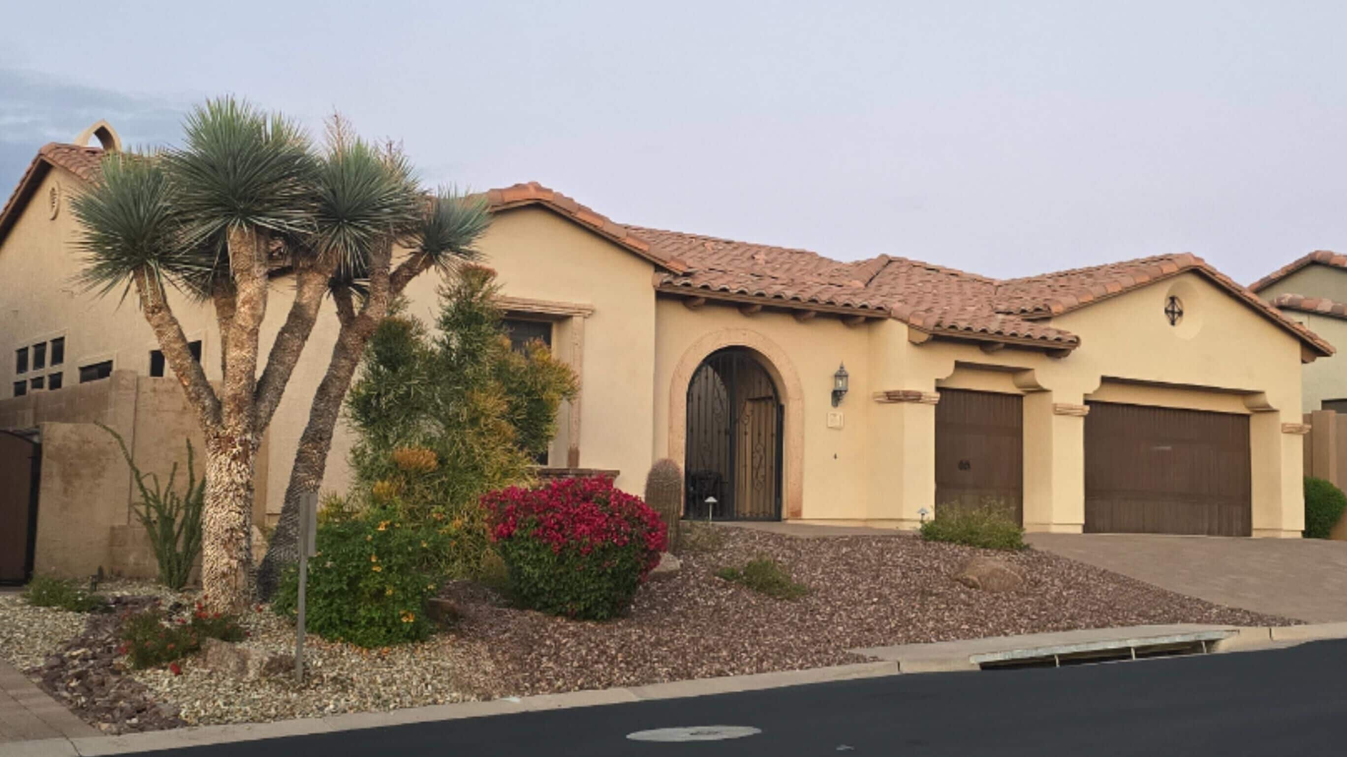 A residential building with a tiled roof, a central arched entrance, and a driveway leading to a garage.