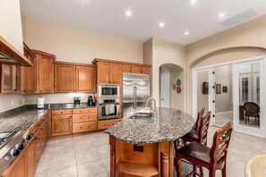 A kitchen with granite countertops, wooden cabinets, stainless steel appliances, and a dining area with chairs. - Experience Refined Desert Living At It's Best! (Mesa)