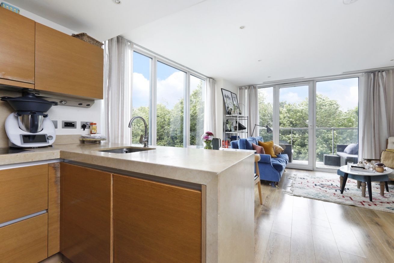 A modern kitchen with a large island, wooden cabinets, and a view of the outdoors through large windows.