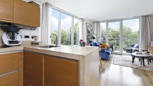 A modern kitchen with a large island, wooden cabinets, and a view of the outdoors through large windows. - Luxury Flat in Chelsea Bridge (Greater London)