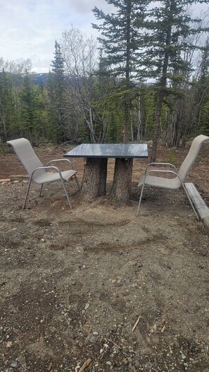 A table set outdoors with metal chairs, surrounded by trees.