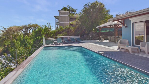 Piscina con sillas de descanso y una terraza, rodeada de árboles y un edificio.