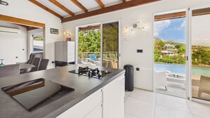 Una cocina moderna con una isla grande, un comedor con sillas y vista a una piscina a través de puertas de vidrio.