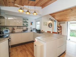 A modern kitchen with white cabinets, a central island, and a wooden ceiling. - Dingle Dell (Braunton)