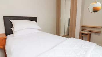 Ein ordentlich bezogenes Bett mit weißer Bettwäsche, ein Nachttisch aus Holz, ein Spiegel an der Wand und ein Holzschrank.