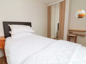 A neatly made bed with white bedding, a wooden nightstand, a mirror on the wall, and a wooden wardrobe. - Dingle Dell (Braunton)