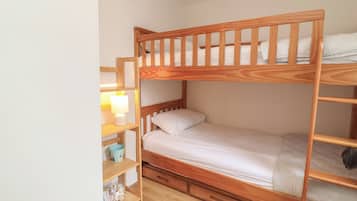 Un lit superposé avec une structure en bois, une table de chevet avec une lampe et une étagère avec des livres et un seau.