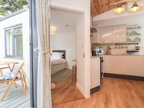 Een kleine kamer met een bed, een tafeltje, een stoel, een kitchenette en een raam.