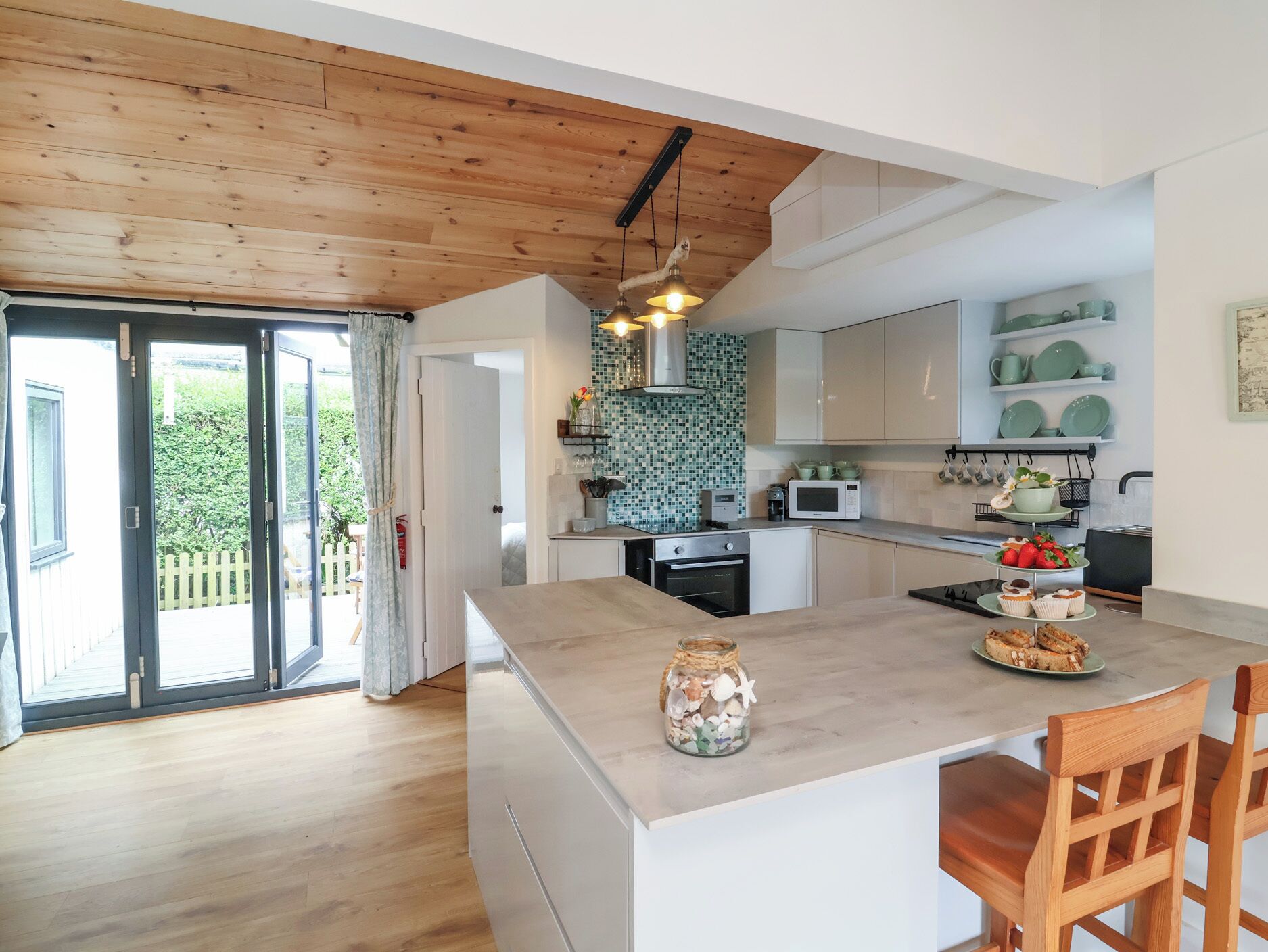 Una cucina moderna con soffitto in legno, un'isola centrale e vista sul verde circostante.