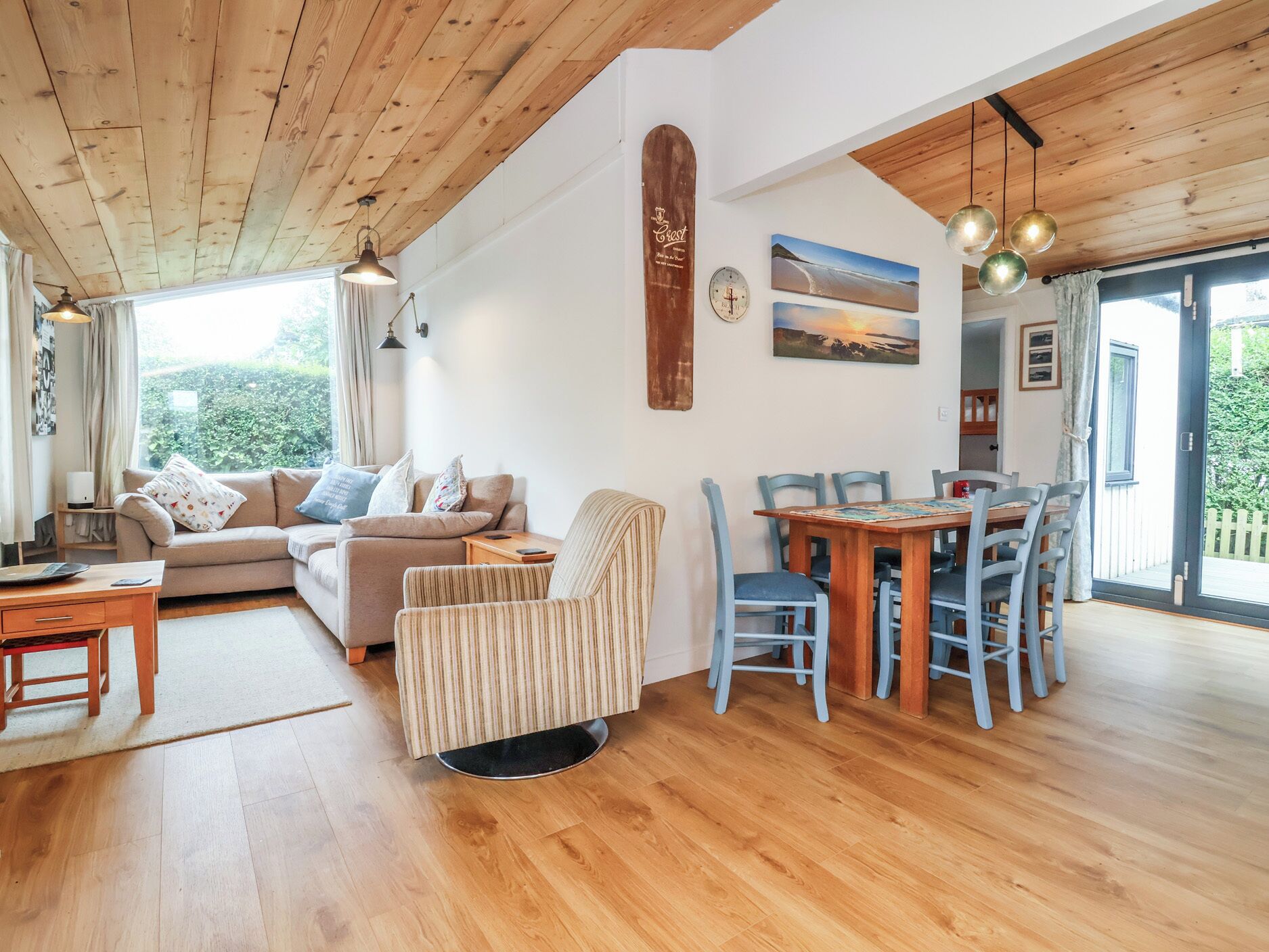 Un accogliente soggiorno con soffitto in legno, un divano, una poltrona a righe, un tavolo da pranzo con sedie e vista sull'esterno.
