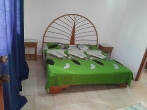 Ein Bett mit grüner Bettdecke und einem Holz-Kopfteil, zwei Nachttische und ein blauer Vorhang.