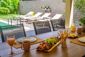 Ein Esstisch mit Obstplatte, Croissants und Grissini vor einer Mauer mit Außenbereich.