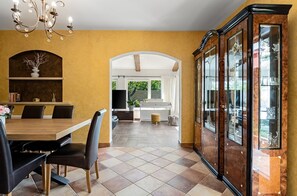 Ein Essbereich mit Holztisch und Stühlen, einer Chandelüster, einem Klavier und einer Vitrine.