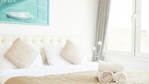 A hotel room with a bed, pillows, a rolled towel, a painting of a boat, and a window with curtains. - Luxury Penthouse, next to Harrods (Londra)