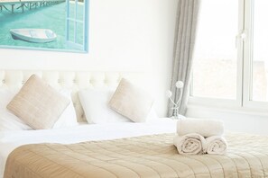 A hotel room with a bed, pillows, a rolled towel, a painting of a boat, and a window with curtains. - Luxury Penthouse, next to Harrods (Londra)