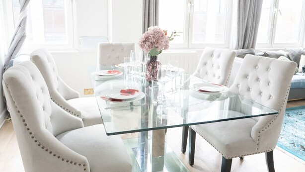 A dining area with a glass table, white upholstered chairs, and a vase with flowers. - Luxury Penthouse, next to Harrods (Londra)