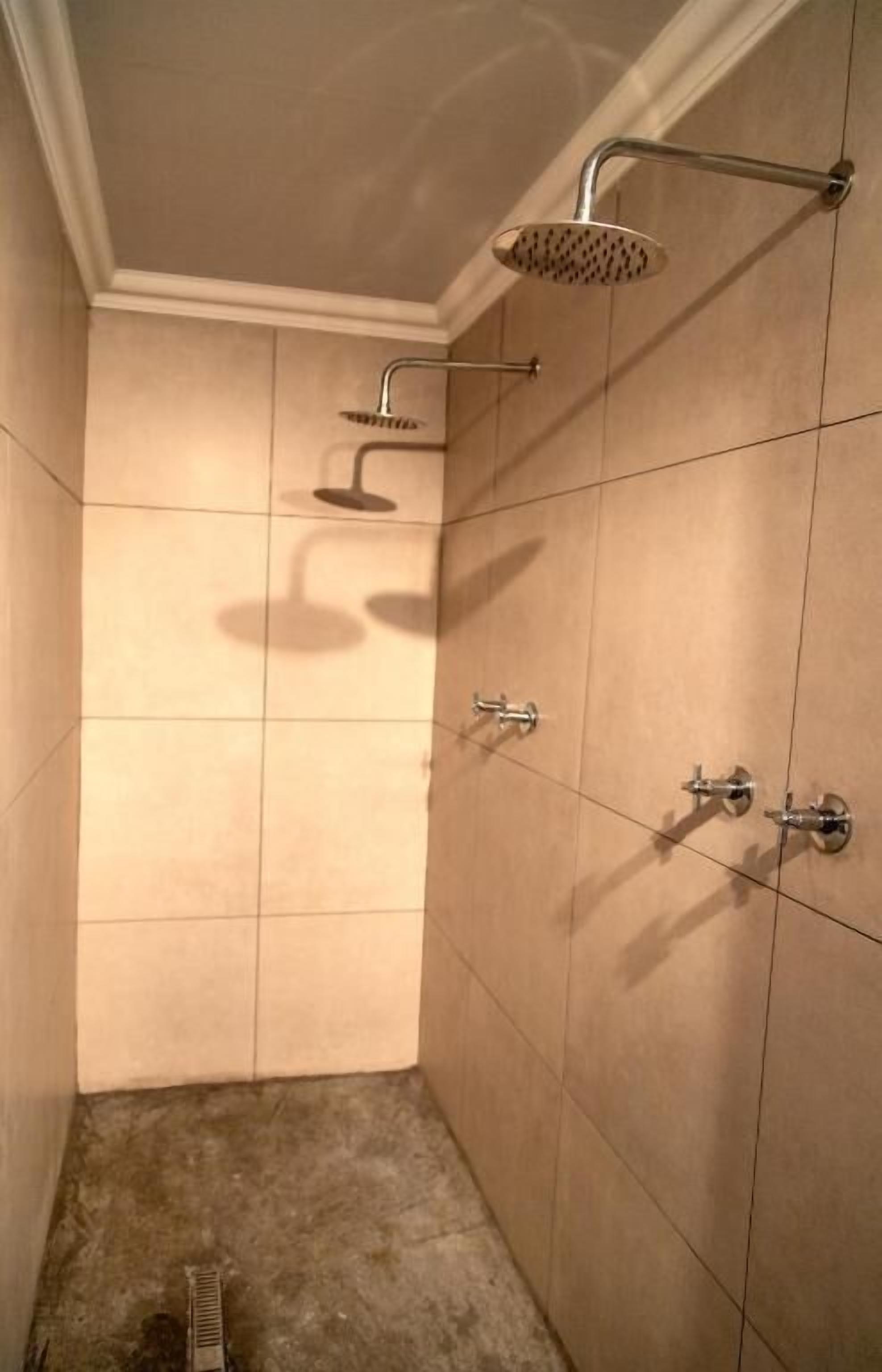Une petite salle de douche carrelée, équipée d’un pommeau de douche à main et d’un robinet mural.