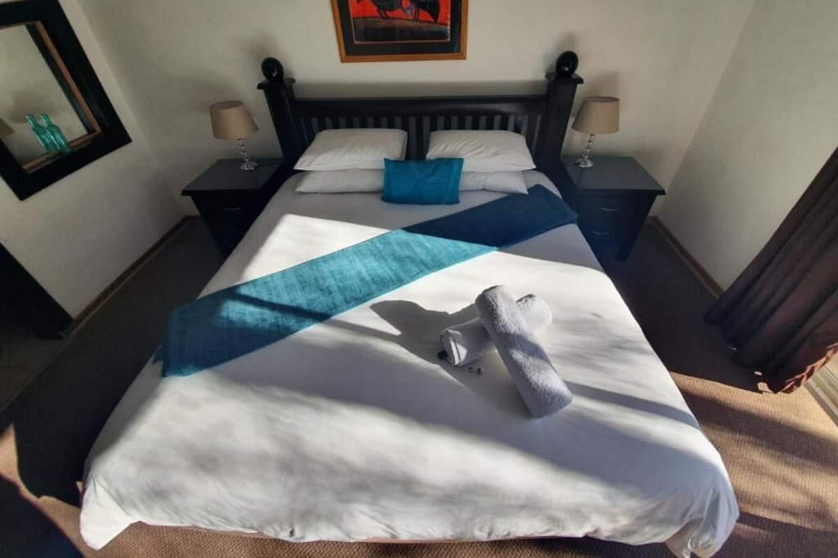 A hotel room with a bed, two bedside tables, a painting on the wall, and a window with curtains.