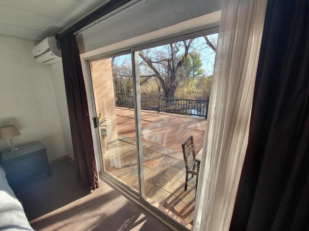 Una habitación con un amplio ventanal corredera que da a un patio exterior con terraza de madera y barandilla de metal.