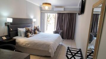 A bedroom with a bed, bedside tables, a chair, a desk, a hanging light fixture, a mirror, and a window with curtains.