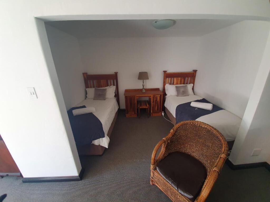 A hotel room with two beds, a small table with a lamp, and a wicker chair.
