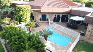 A house with a swimming pool, surrounded by a white fence, and a covered patio area.