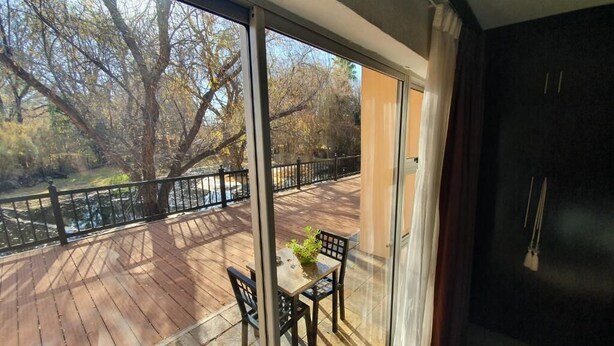 A balcony with a wooden deck, a table with chairs, and a view of trees and a body of water.