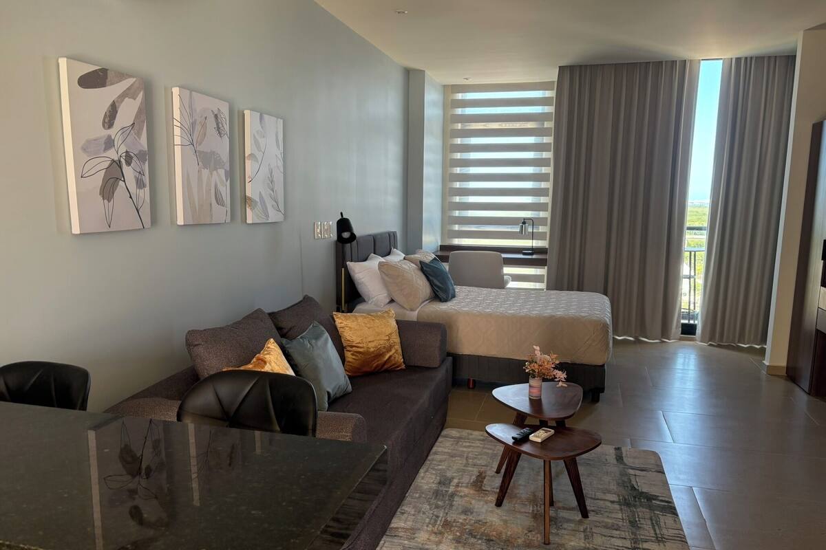 A modern hotel room with a bed, sofa, and dining area.