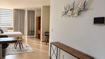 Quarto de hotel moderno com cama, escrivaninha, cadeira, mesa pequena e um objeto decorativo na parede.
