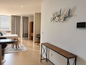 A modern hotel room with a bed, a desk, a chair, a small table, and a decorative wall piece.