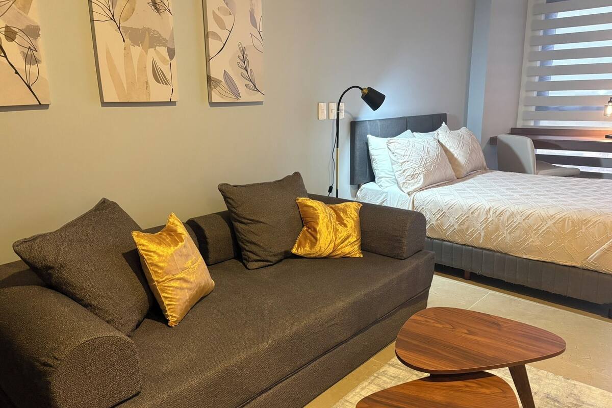 A modern bedroom with a dark brown sofa, a wooden coffee table, and a bed with white bedding.