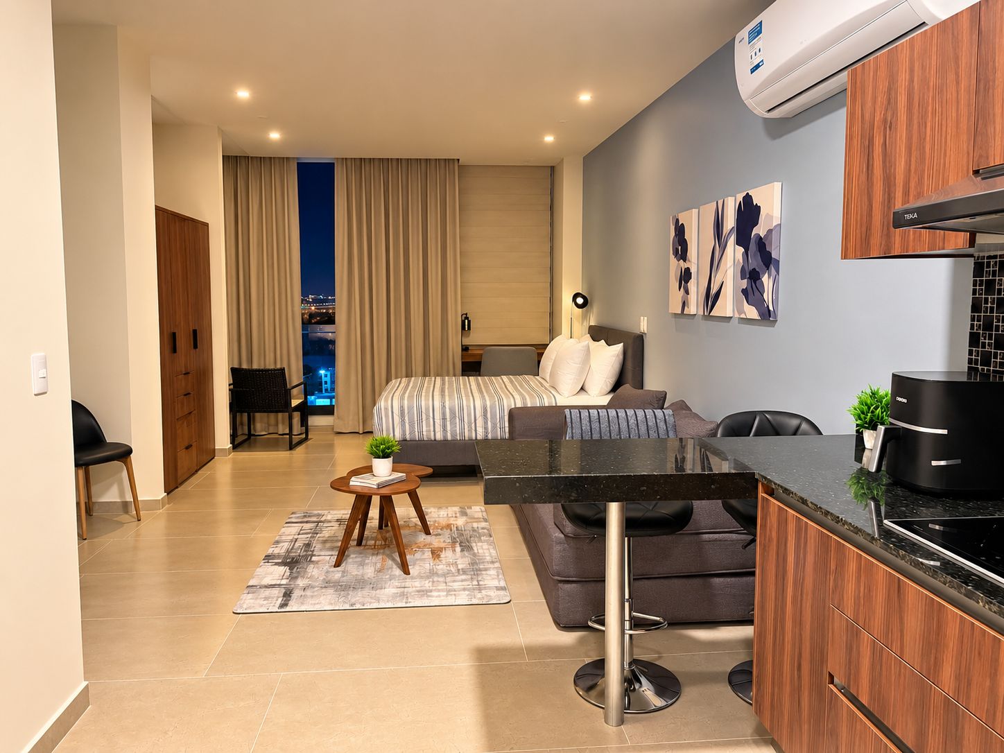 Un apartamento moderno con kitchenette, comedor, sala de estar con sofá y cama, y vistas de la ciudad por la noche.