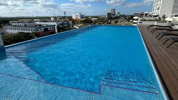 Uma piscina no terraço com água azul cristalina, rodeada por edifícios e um céu limpo.