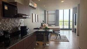 Uma cozinha moderna com cafeteira, área de refeições com sofá e mesa, e varanda com vista.
