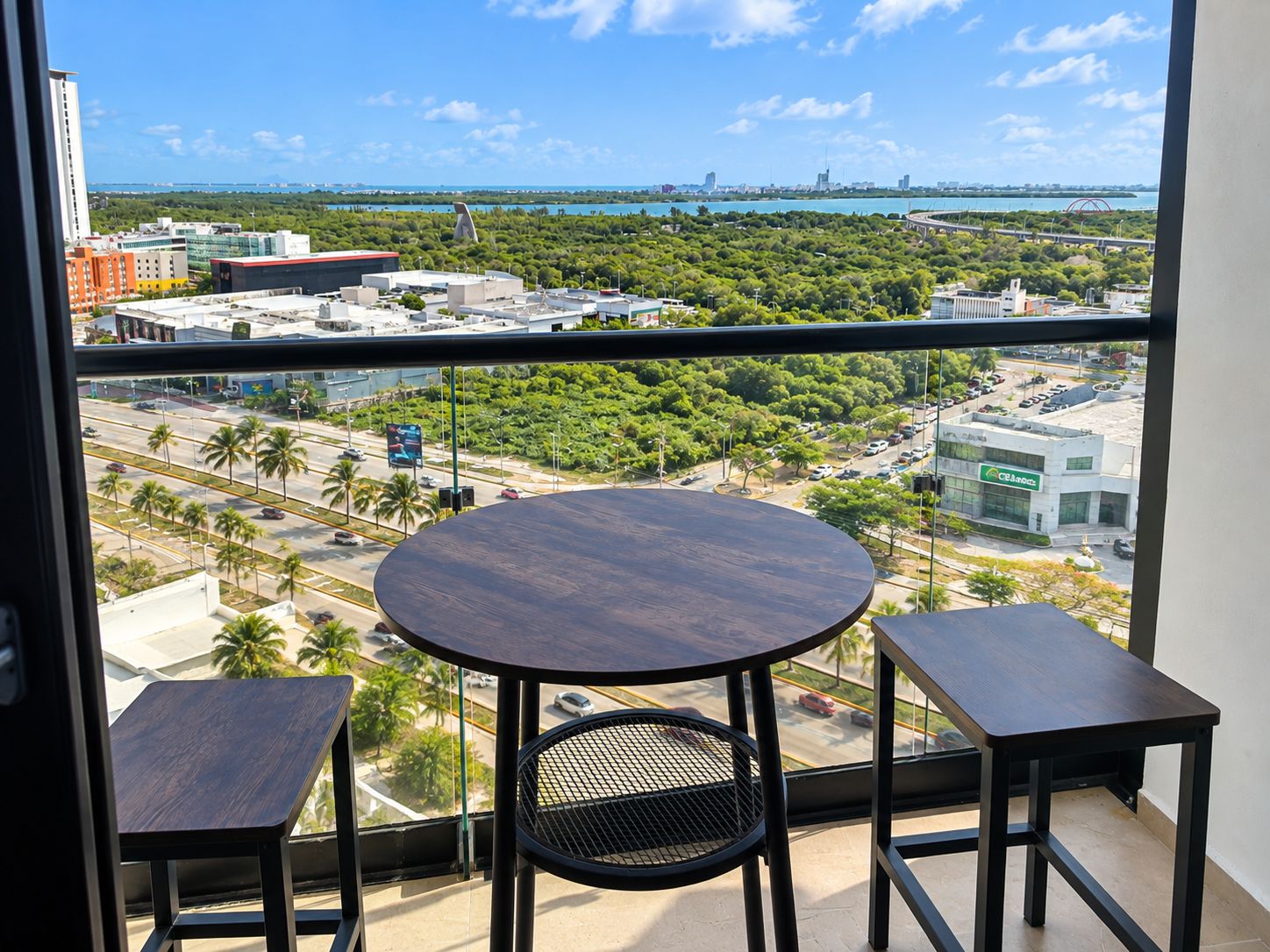 A balcony with a round table and two chairs, overlooking a cityscape with buildings and a bridge.