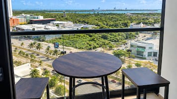 A balcony with a round table and two chairs, overlooking a cityscape with buildings and a bridge.