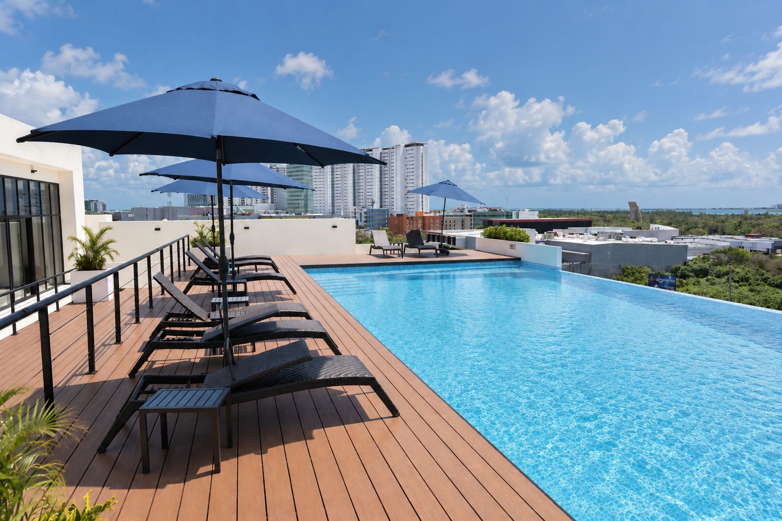 A rooftop pool with lounge chairs and umbrellas, surrounded by modern buildings and a clear sky.