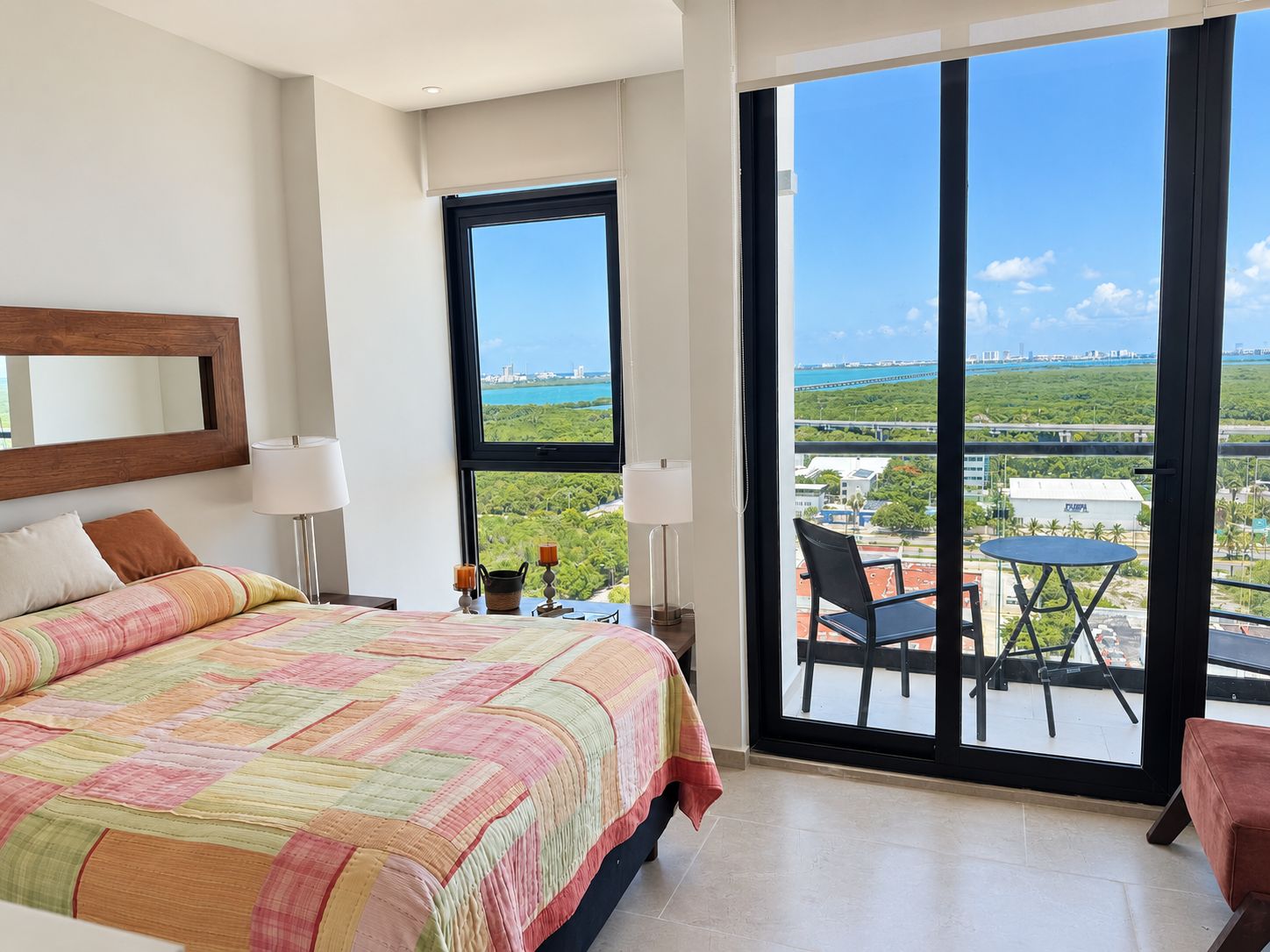 Een hotelkamer met een groot bed, uitzicht op de stad en een balkon met een tafel en stoelen.