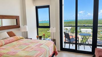 Een hotelkamer met een groot bed, uitzicht op de stad en een balkon met een tafel en stoelen.