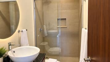 Un baño moderno con ducha envuelta en vidrio, un lavabo blanco y un inodoro.